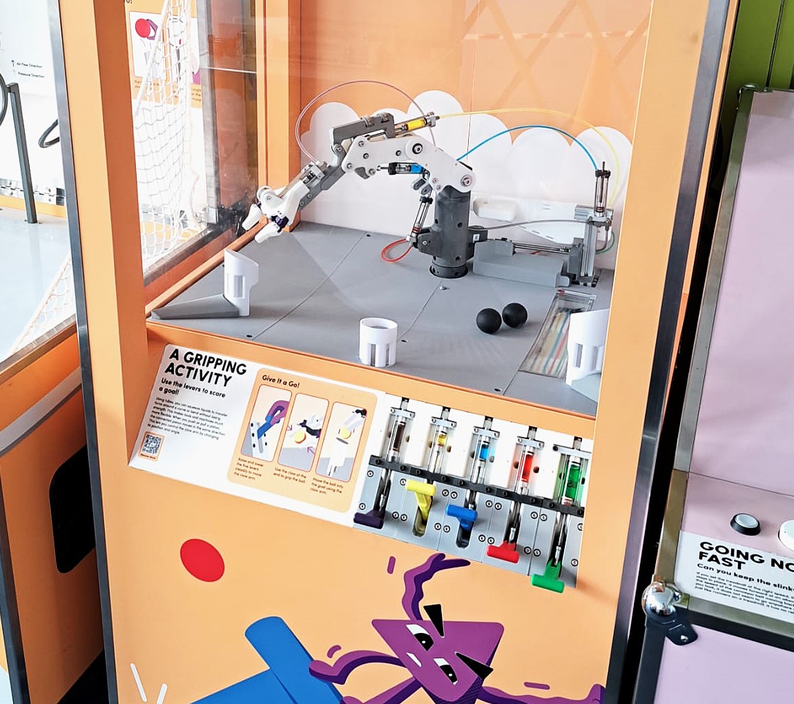 Children using the hydraulic arm interactive exhibit to pick up a ball